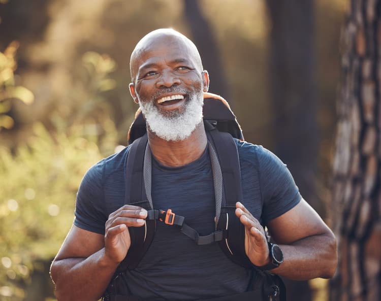 An older man smiling on a sunlit forest hike