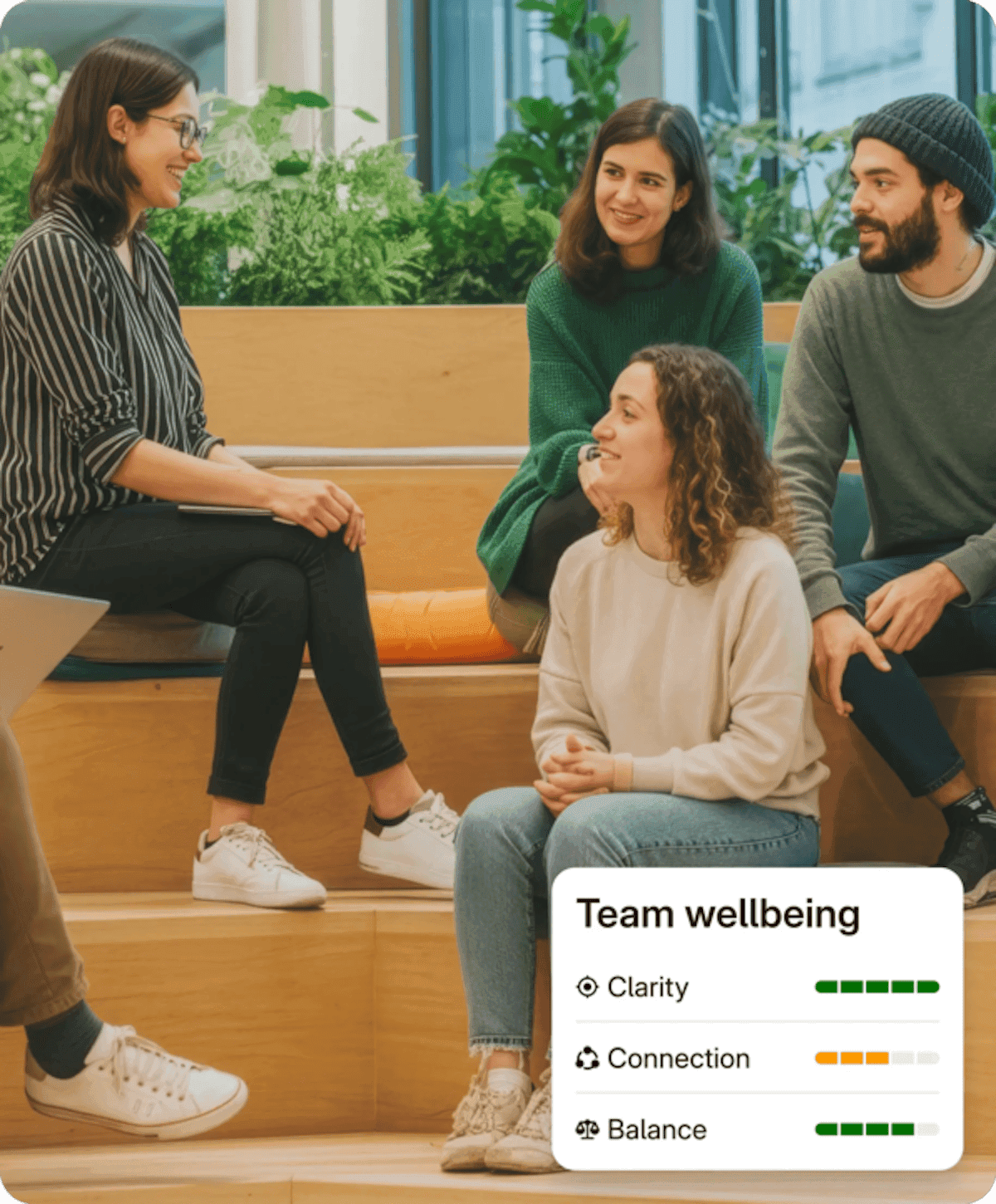 A small group in warm conversation in a bright lounge, a wellbeing scorecard beside them